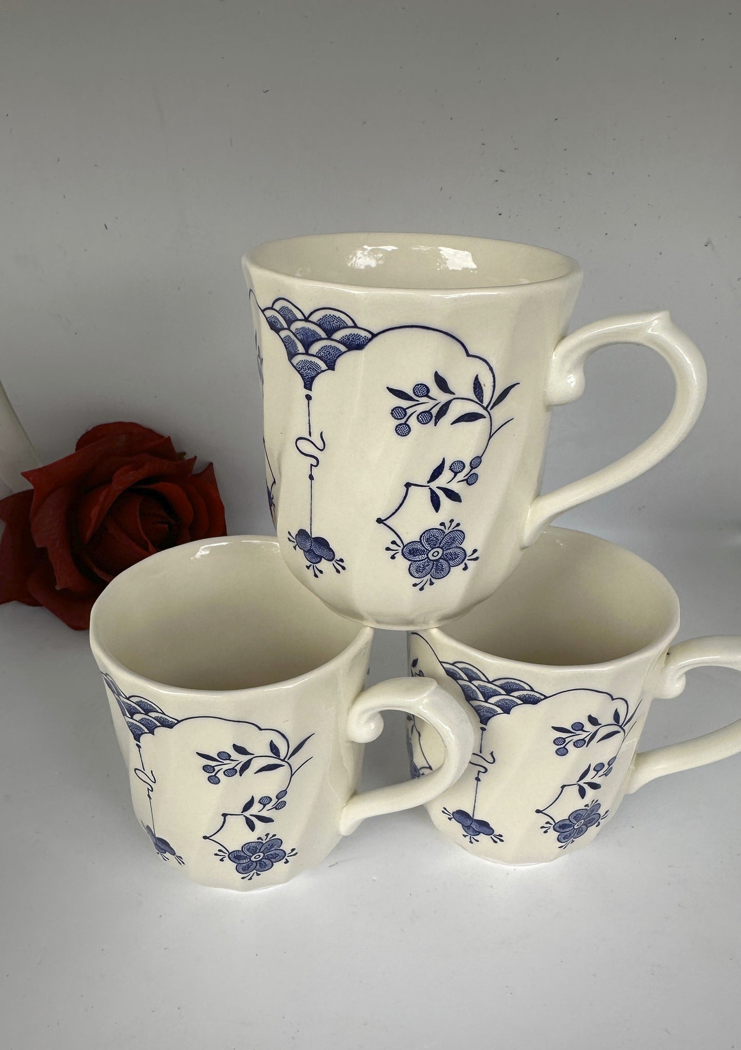 A set of 4 white ceramic mugs with blue floral designs and a swirl rim, displayed against a neutral background.