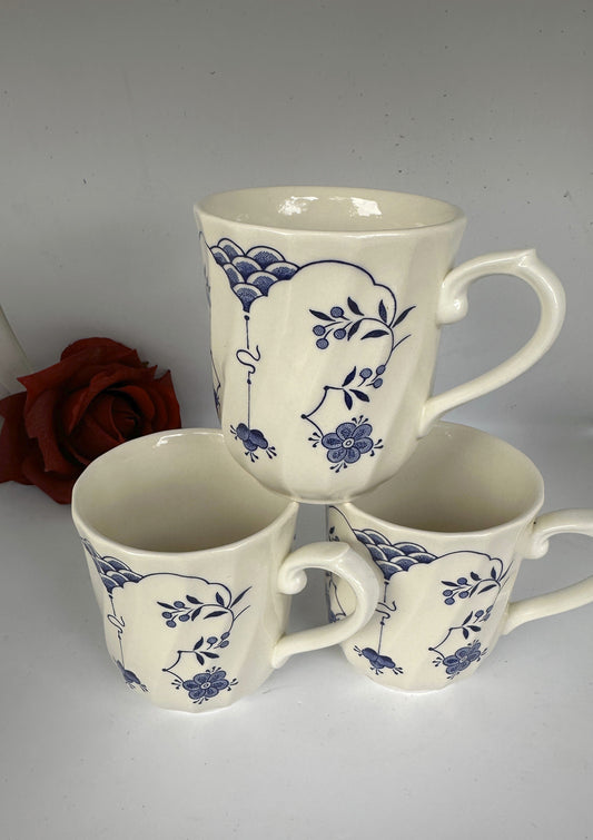 A set of 4 white ceramic mugs with blue floral designs and a swirl rim, displayed against a neutral background.