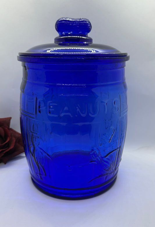 A cobalt blue glass jar with a lid, featuring an embossed design and the Planters Mr. Peanut logo.