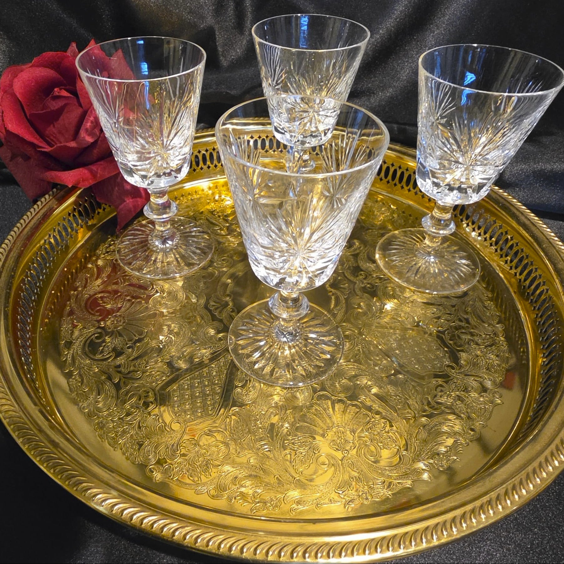 Four crystal glasses on a gold tray with a red rose against a black background