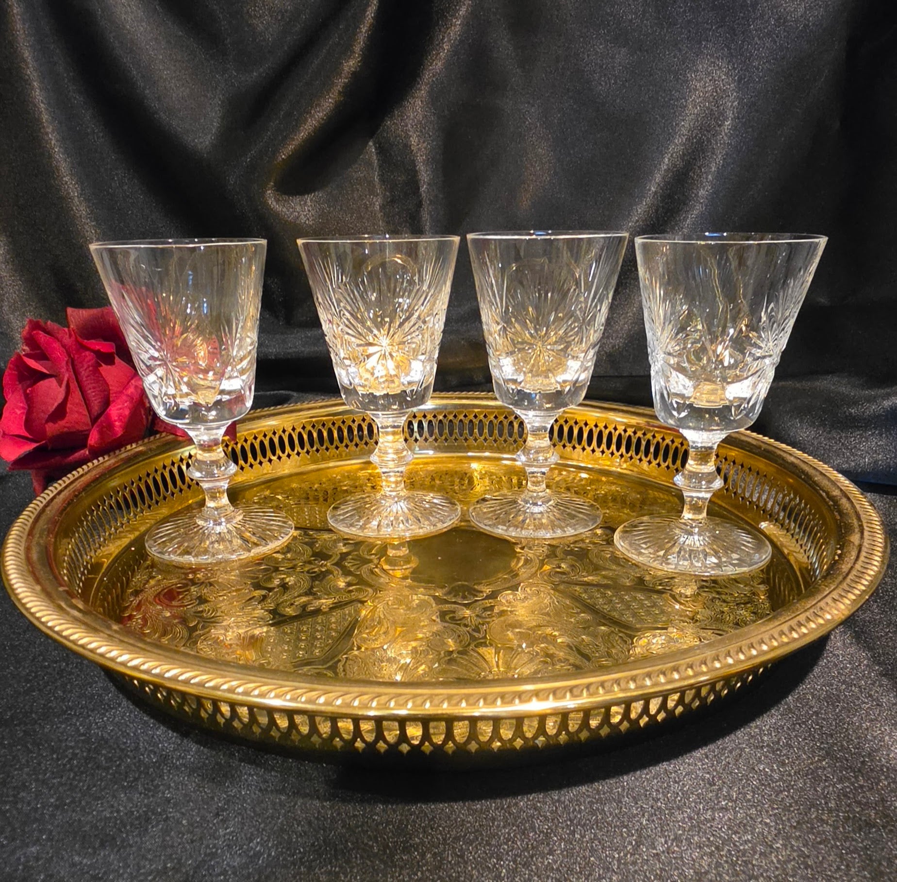 Four crystal glasses on a gold tray with a red rose against a black background